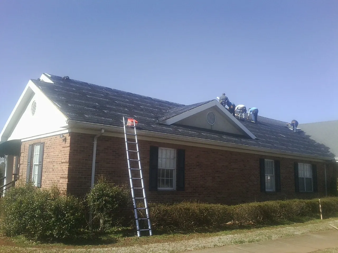 Crew tearing shingles off a brick ranch roof with a ladder set — Metal Roof Repair work by our crew in Findlay