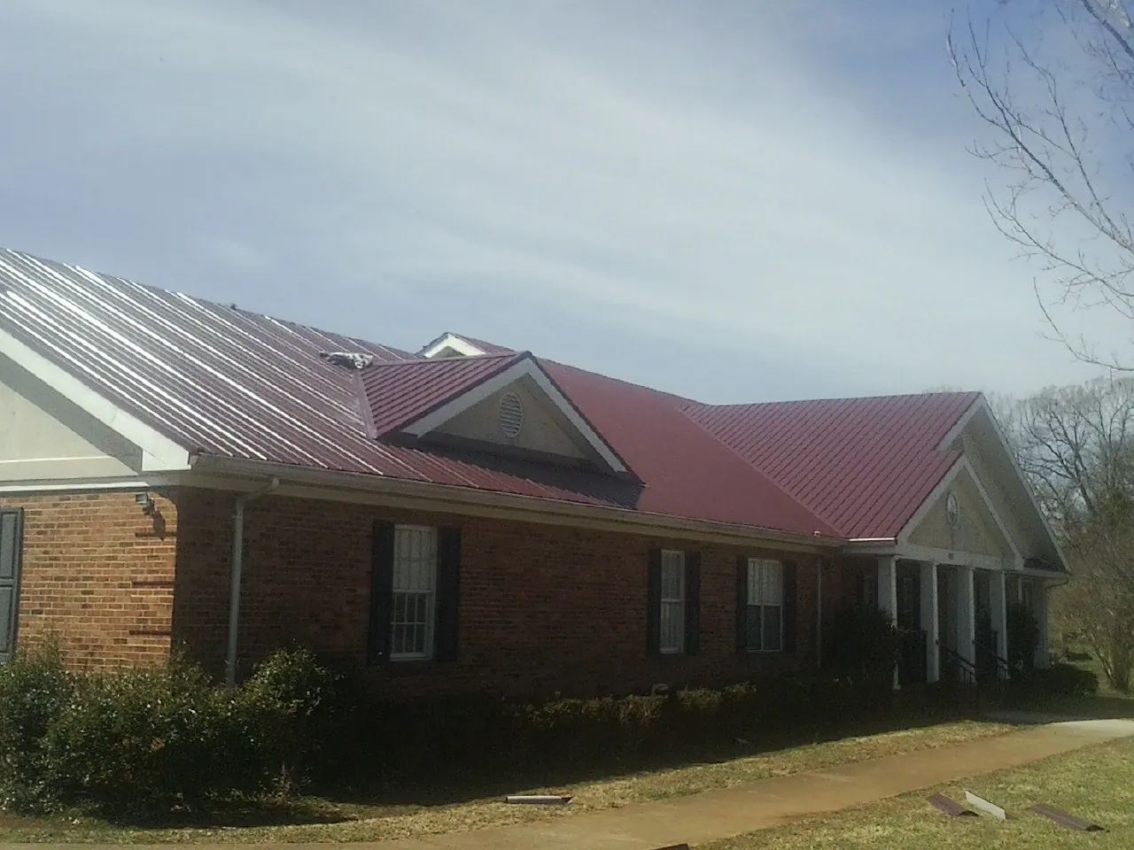 Red metal roof with gabled entries on a long brick building, from a Hail Damage Roof Repair job in Findlay