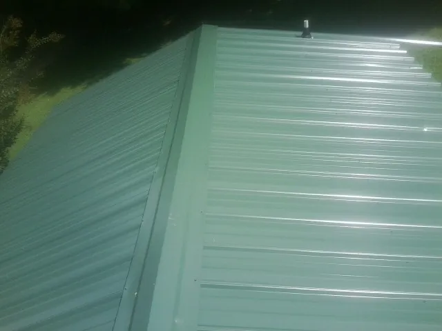 New green metal panels meeting at the ridge of a roof — Flat Roof Repair work by our crew in Findlay