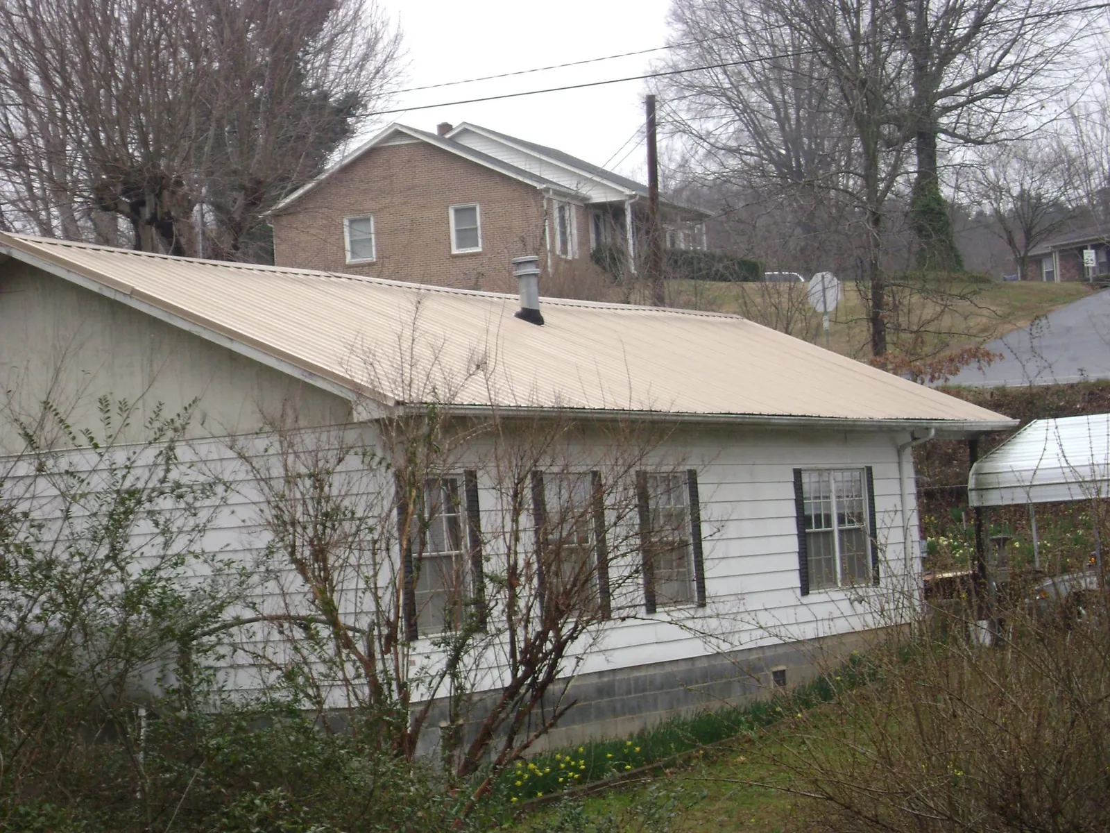 Tan metal roof on a white sided house set into a hillside — Commercial Roofing by Roofing Brothers in Findlay